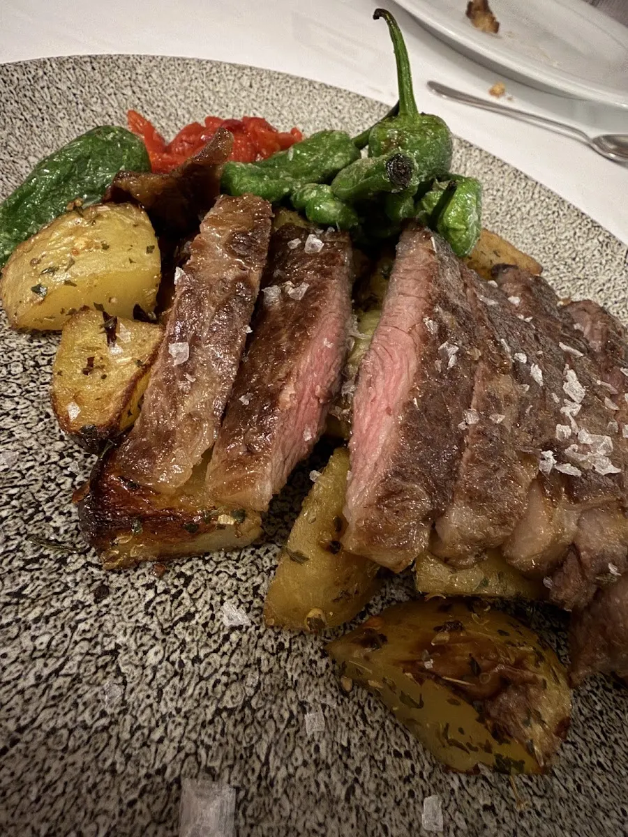 Carne a la brasa cortada en tiras con escamas de sal, patatas asadas y pimientos verdes