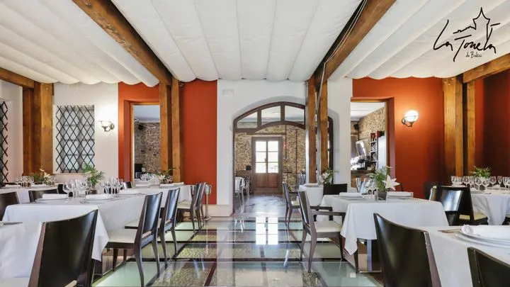 Comedor con vigas de madera, paredes rojas, toldo blanco en el techo y mesas vestidas con mantel blanco