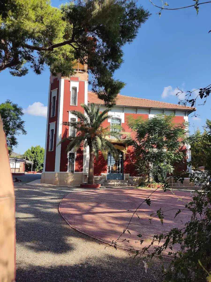 La villa de La Torreta de Beltrí: fachada roja con molduras blancas, la torre de tres alturas, una palmera y pinos en el patio