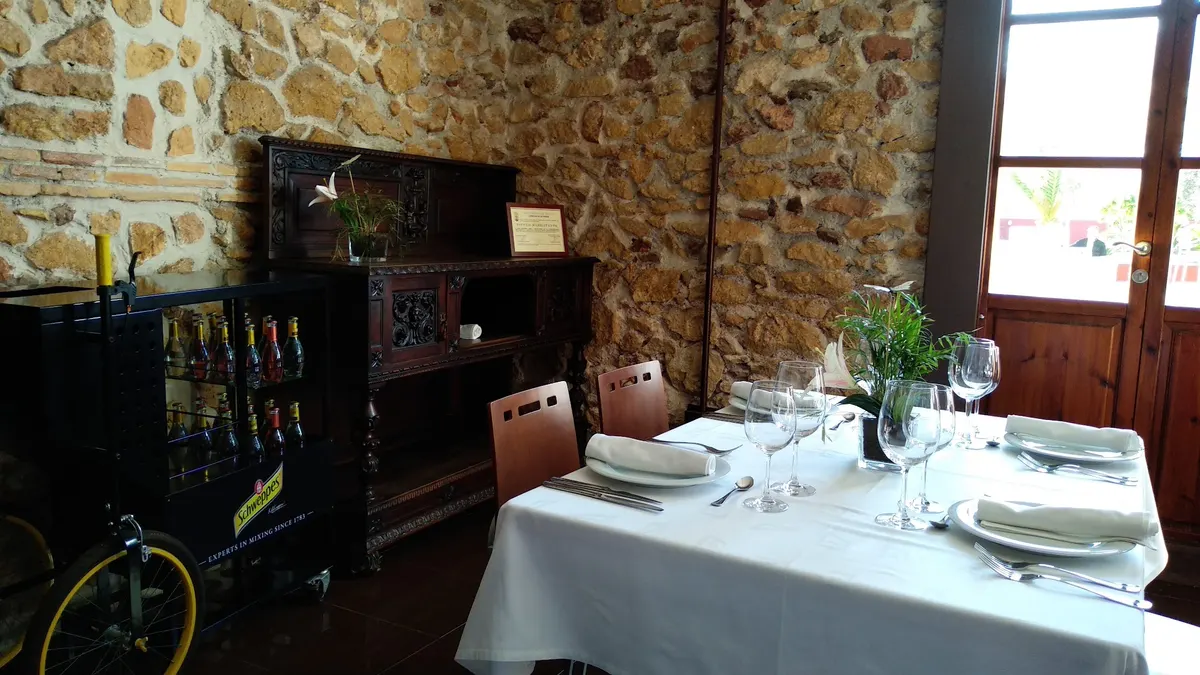 Sala con muros de piedra vista, ventanas de madera y una mesa puesta con flores y copas